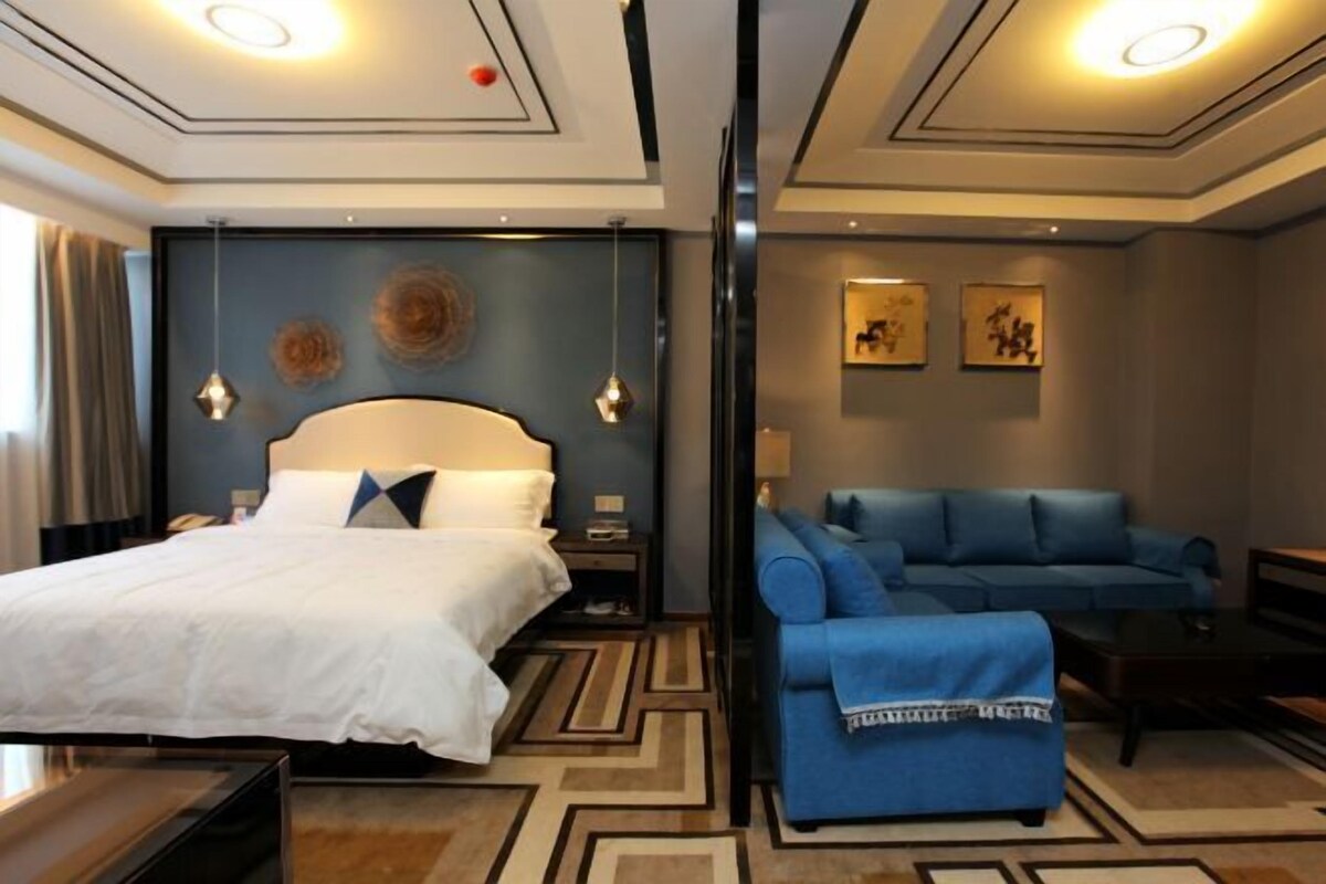 A hotel room with a large bed, a blue sofa, a small table, and a wall with framed artwork.