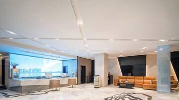 A modern hotel lobby with a reception desk, seating area, and a large digital screen displaying a cityscape.