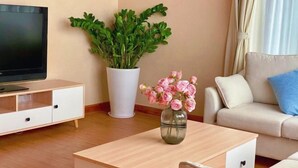 A living room with a TV, a white cabinet, a plant, a vase with flowers, and a sofa. - Luzui Hotel (Shenzhen)