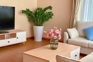 A living room with a TV, a white cabinet, a plant, a vase with flowers, and a sofa. - Luzui Hotel (Shenzhen)