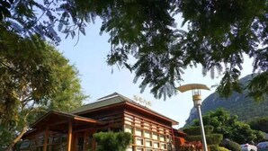 A traditional wooden building with a sign above the entrance, surrounded by lush greenery and a mountainous backdrop. - Luzui Hotel (Shenzhen)