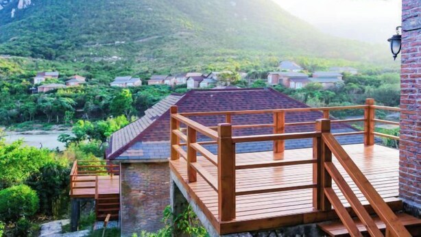 A wooden deck with a brick wall, overlooking a mountainous landscape with houses. - Luzui Hotel (Shenzhen)