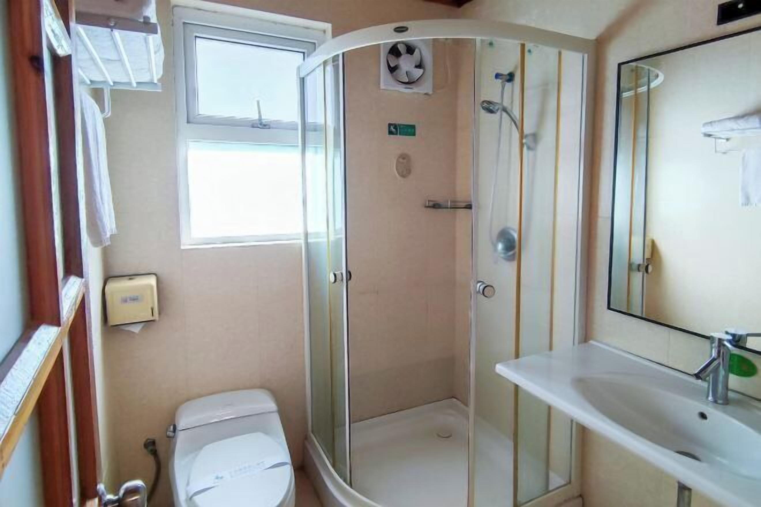 A bathroom with a shower, toilet, sink, and a window.