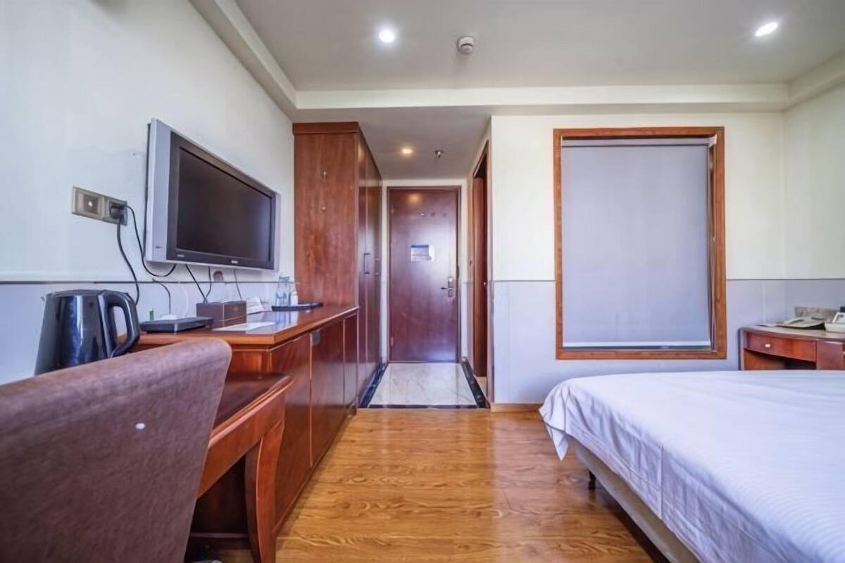 A hotel room with a wooden desk, a television, a bed, and a sliding door.