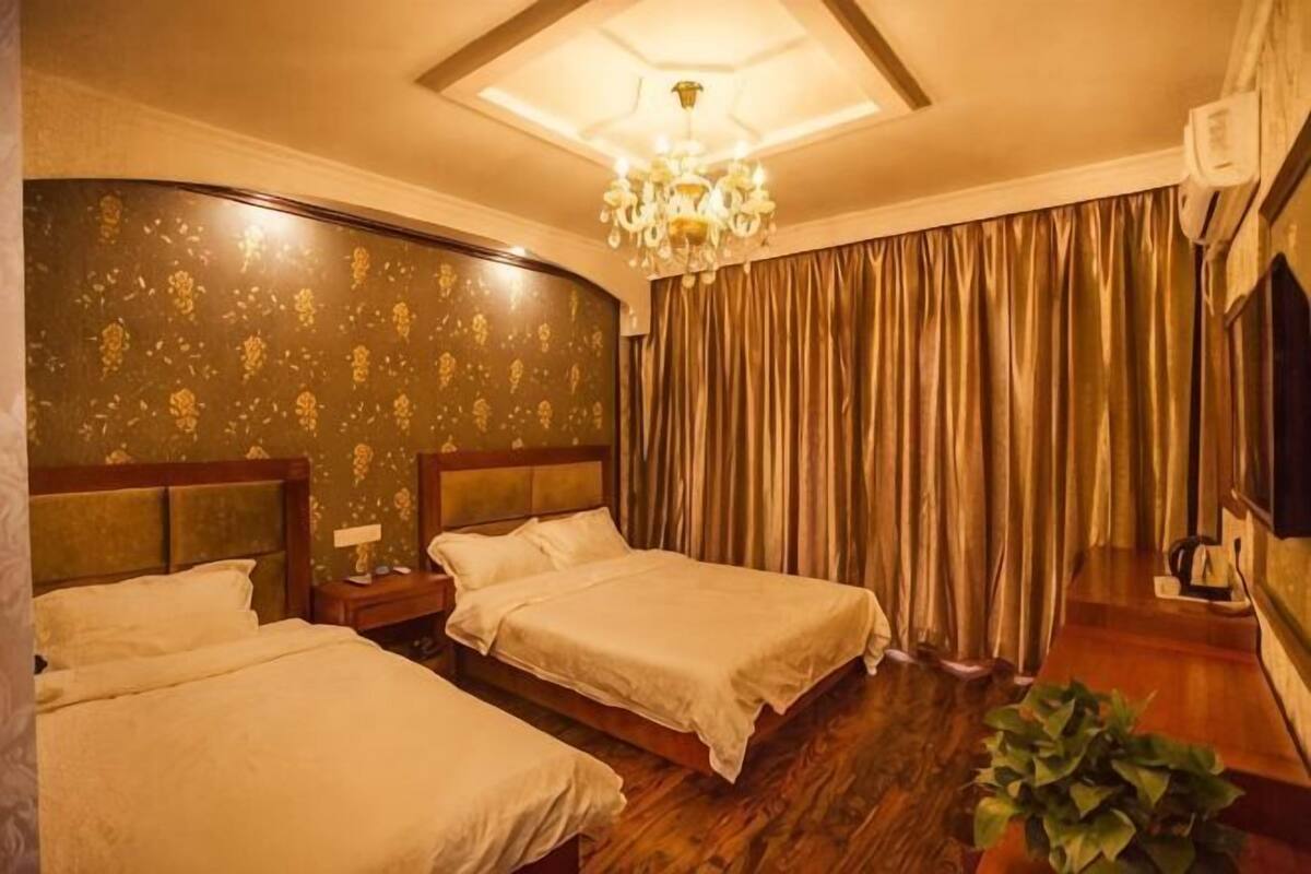 A hotel room with two beds, a chandelier, a large window with curtains, and a television.