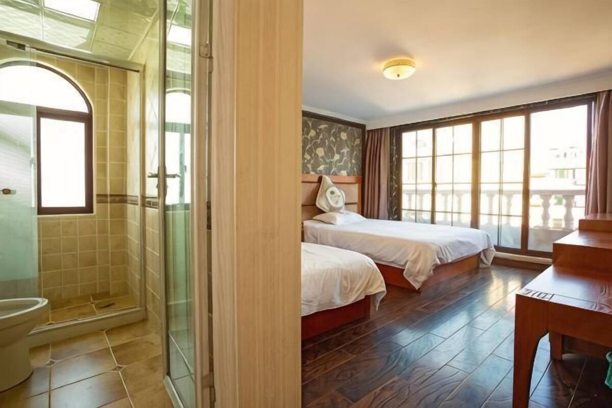 A hotel room with a shower, two beds, a dining table, and large windows.