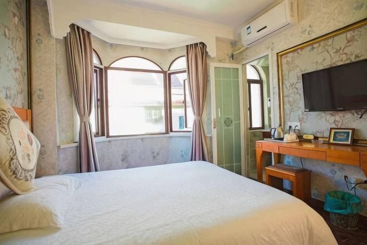 A hotel room with a bed, a desk, a television, and a window with curtains.
