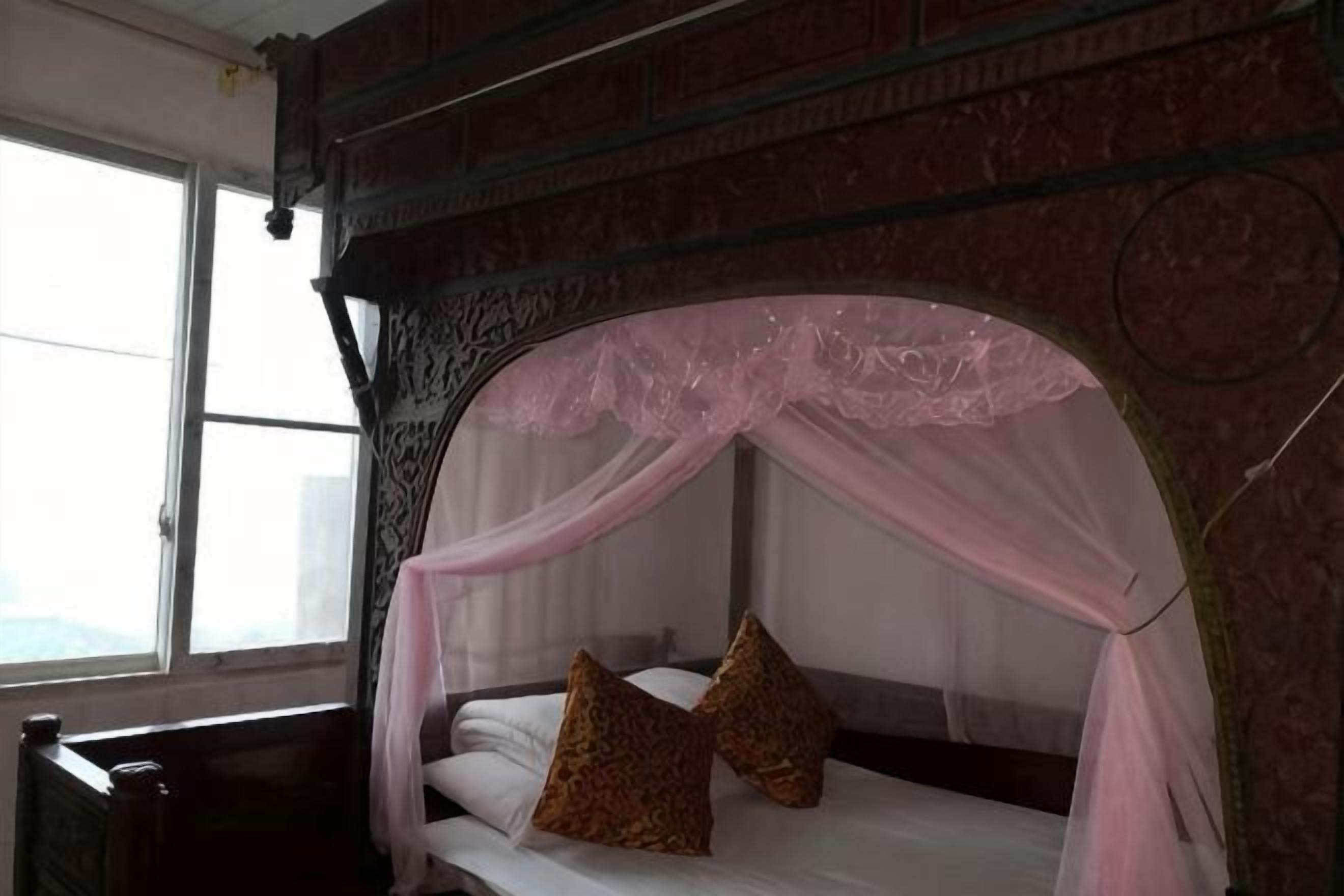 A bed with a canopy, a window, and a brick wall.