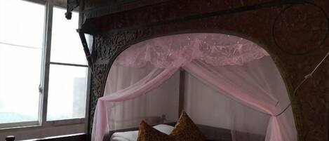 A bed with a canopy, a window, and a brick wall.
