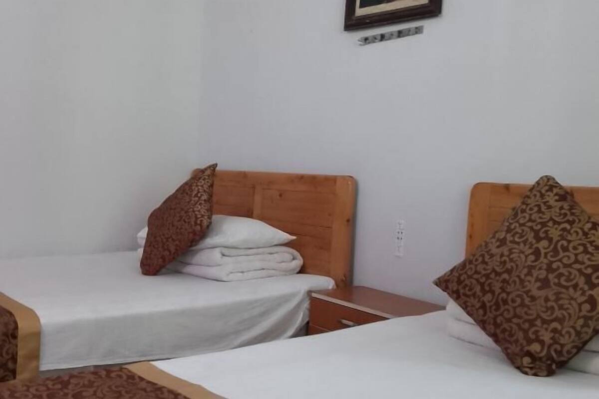 A hotel room with two single beds, wooden headboards, white bedding, and patterned pillows.