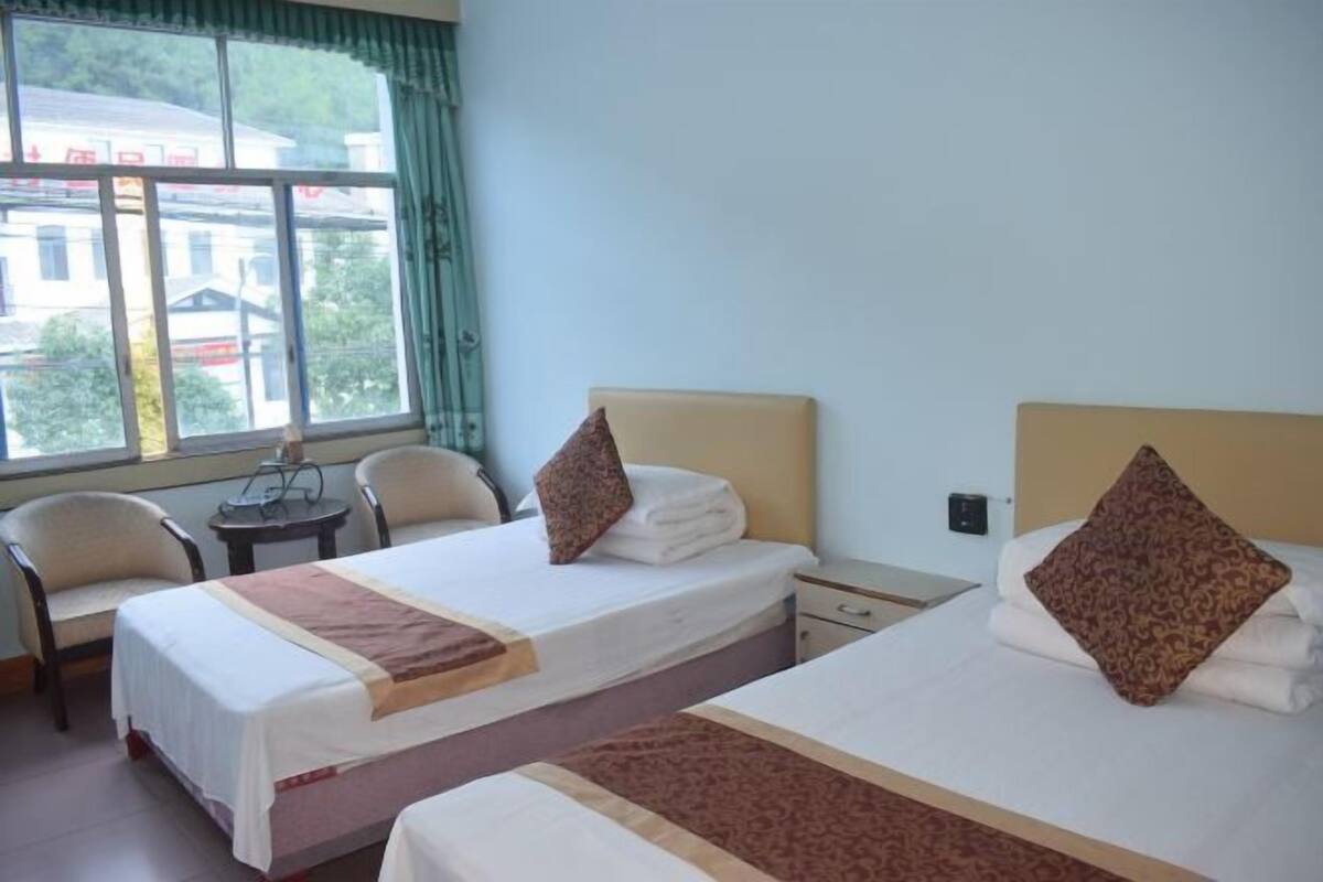 A hotel room with two beds, a window with curtains, a small table, and two chairs.