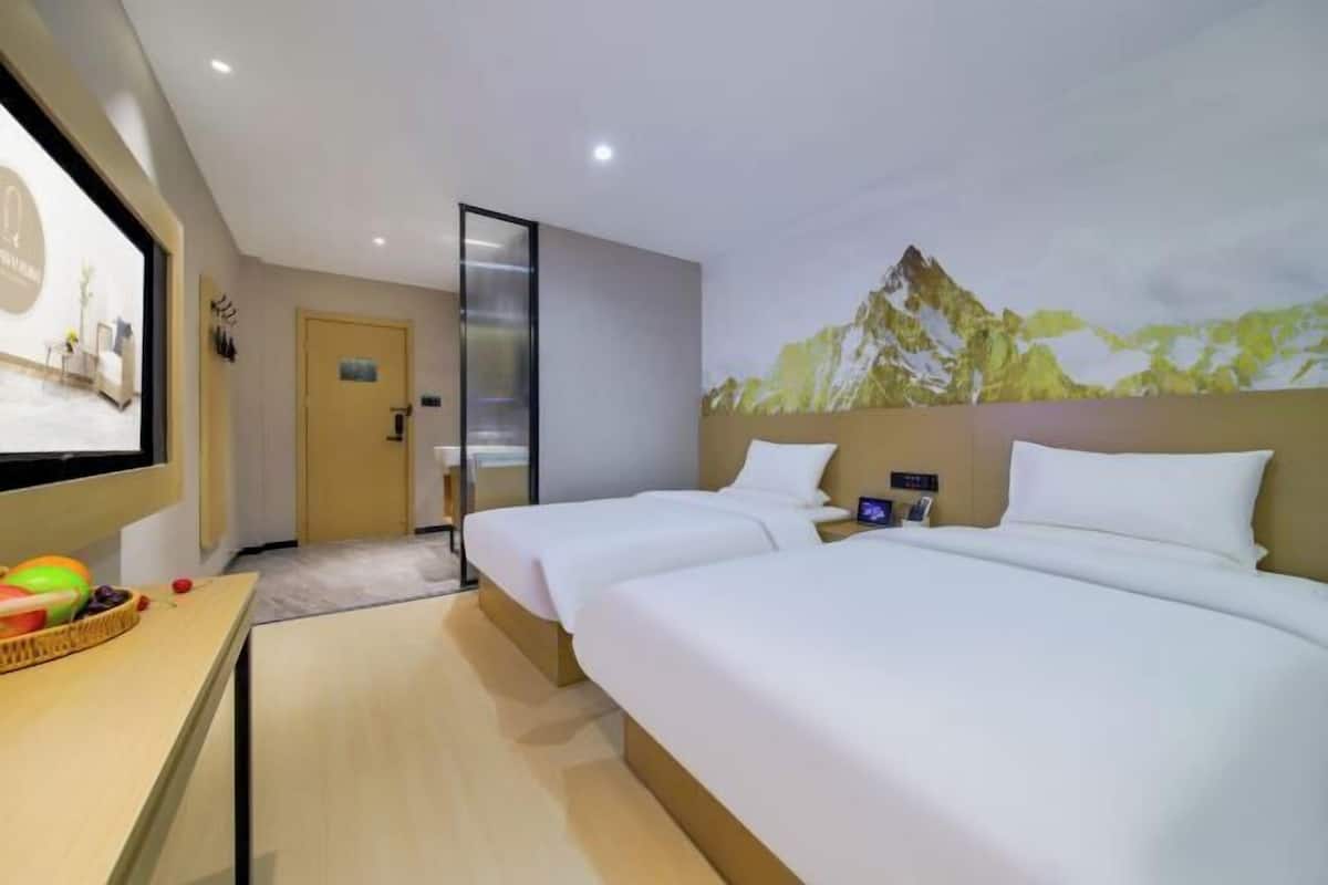 Une chambre d’hôtel avec deux lits, une télévision, un bureau agrémenté d’un panier de fruits et une fresque murale représentant un paysage de montagne.