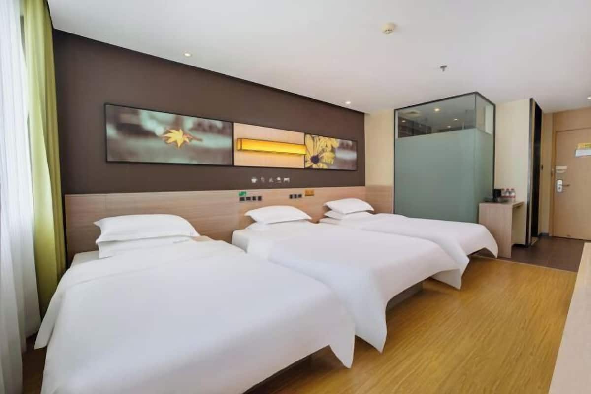 Une chambre d’hôtel avec trois lits, une grande œuvre d’art murale, un petit bureau et une cloison en verre.