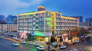 A multi-story hotel with a modern design, featuring a prominent green sign on the facade and several ground-level commercial spaces. - Iu Hotel Zhengzhou Science Avenue Zhengzhou University (Zhengzhou)