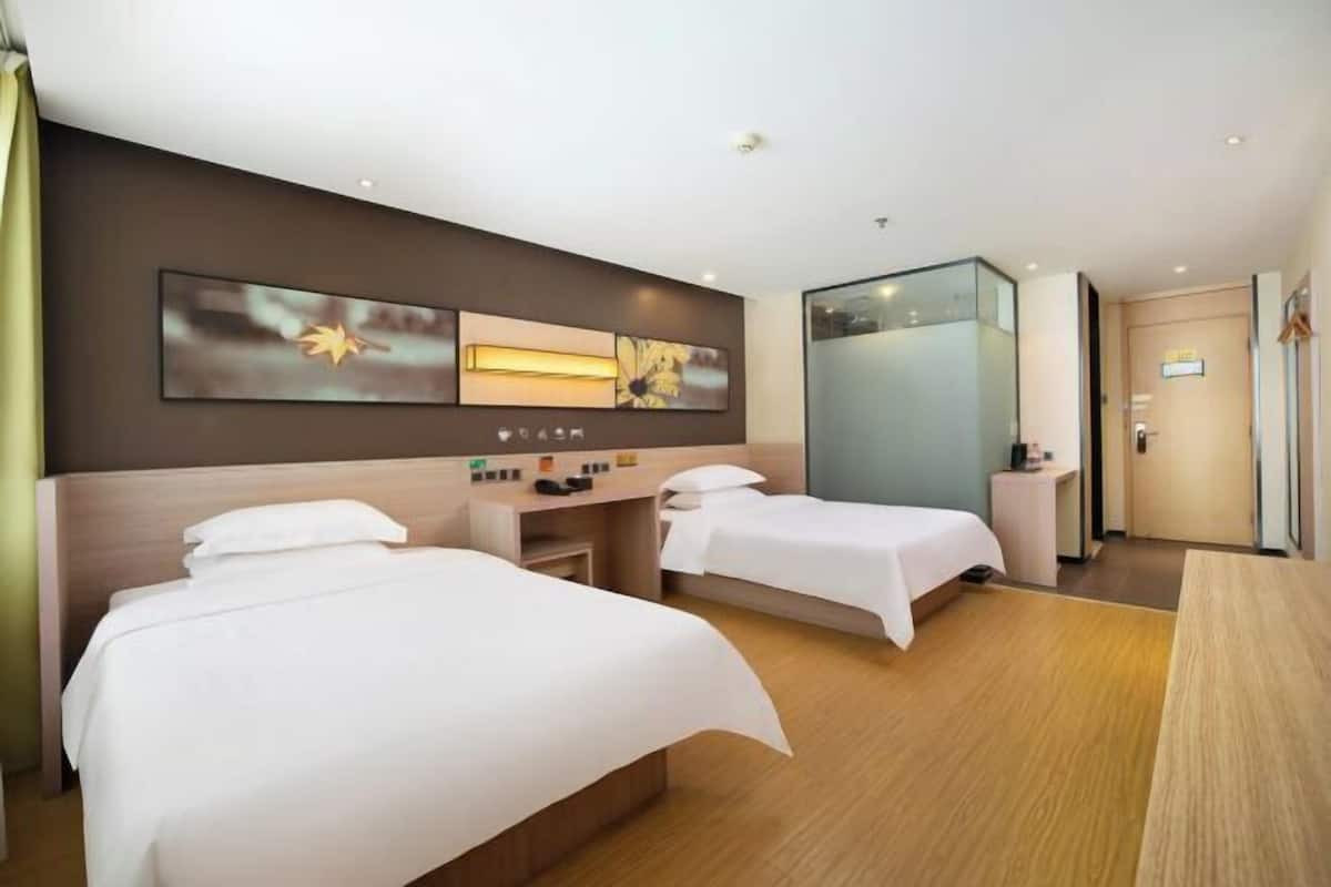 Une chambre d’hôtel avec deux lits, un bureau, un miroir et des œuvres d’art accrochées au mur.