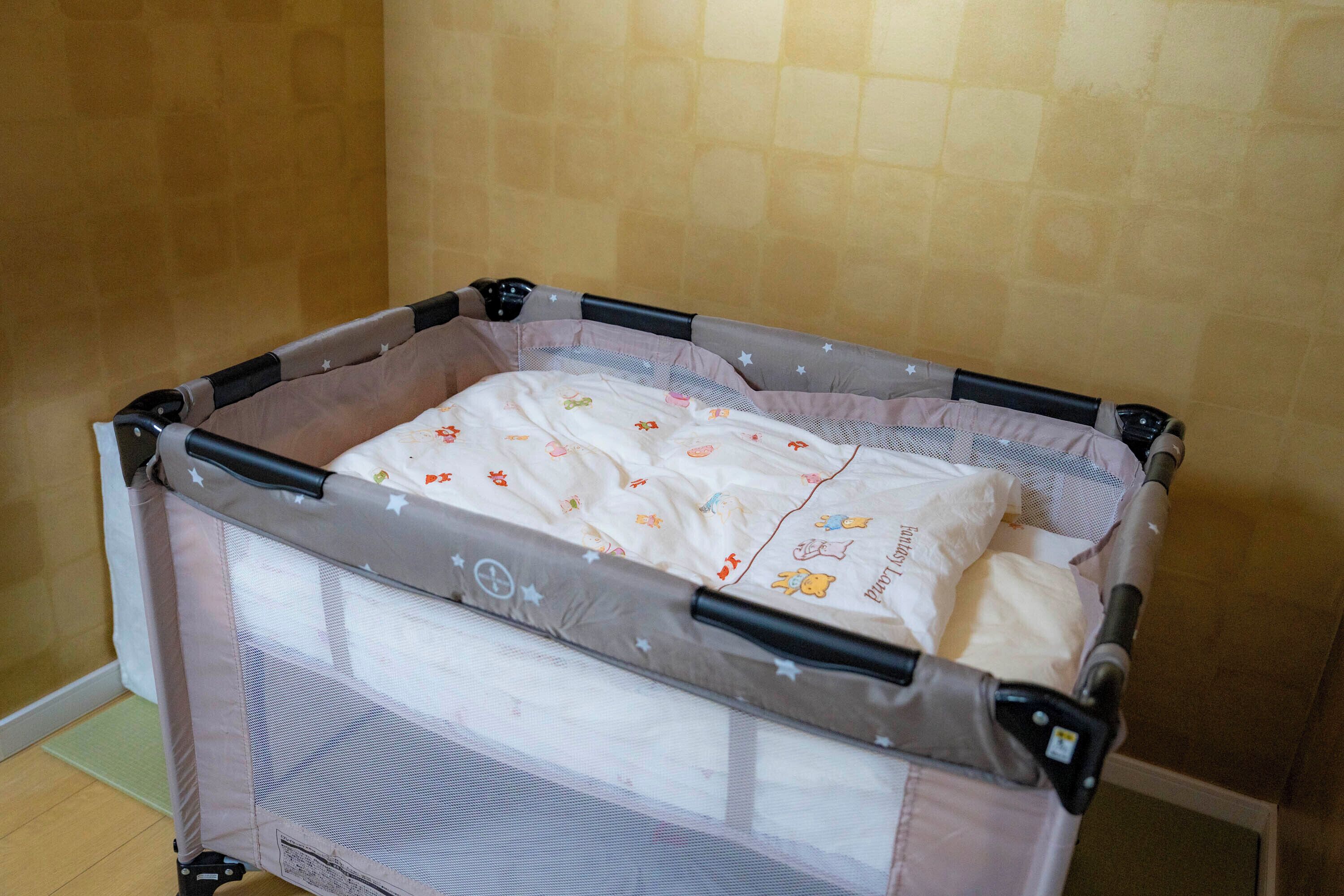 A portable crib with a mesh side and a padded mattress, set against a wall with a textured pattern.