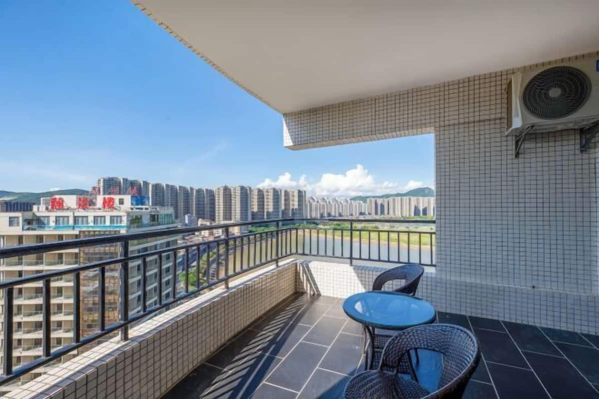Ein Balkon mit Blick auf hohe Gebäude, ein Tisch mit Stühlen und eine Klimaanlage.