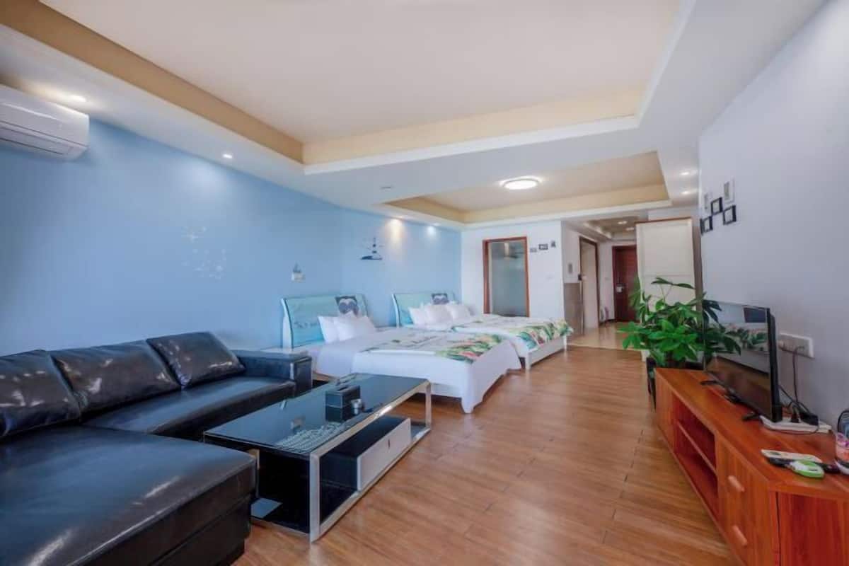 Ein modernes Hotelzimmer mit einer Couch, einem Bett mit Blumenmuster, einem Holztischchen, einem Fernseher auf einem Holzständer und einer Zimmerpflanze.