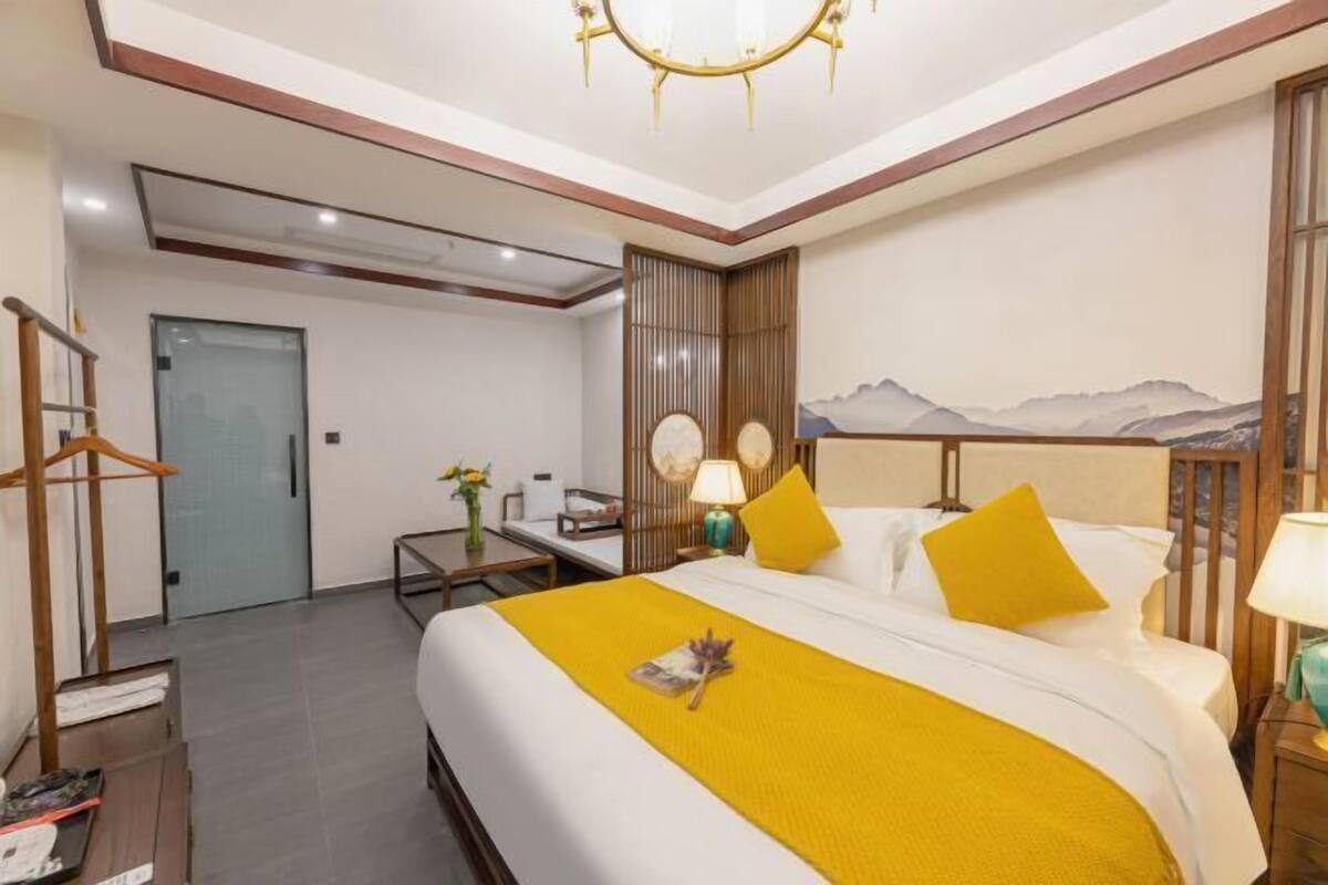 Una habitación de hotel con cama, mesitas de noche, un escritorio, una silla, una lámpara y un cuadro de paisaje montañoso en la pared.