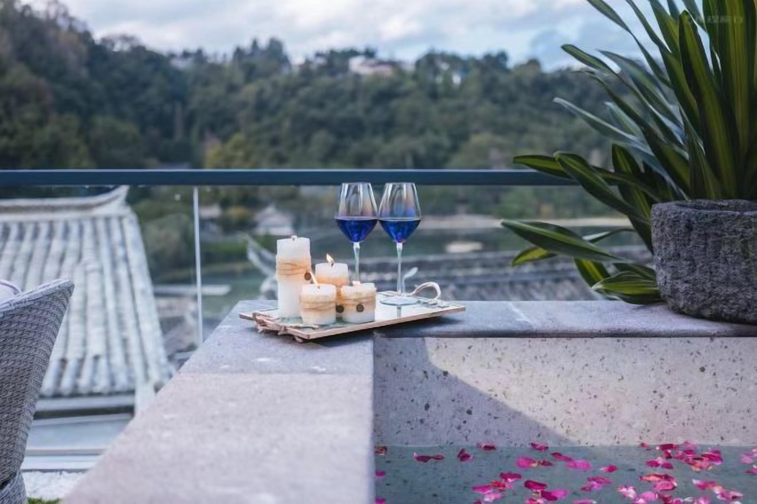 Un balcón con una mesa dispuesta con velas y copas, con vistas a un paisaje pintoresco.