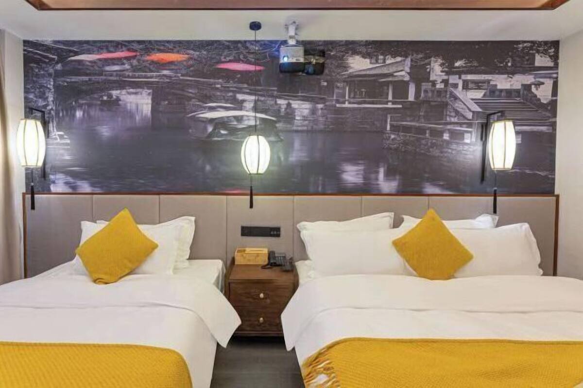 Habitación de hotel con dos camas, una mesita de noche, un proyector montado en la pared y un gran mural con motivo acuático.