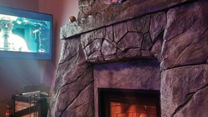 A stone fireplace with a fire, a television mounted on the wall, and a fire extinguisher. - Rustic elegance (St Malo)