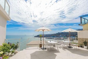 Eine Terrasse mit Gartenmöbeln, Blick aufs Meer und einem Geländer.