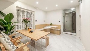 Ein modernes Zimmer mit einem Holztisch, einer Bank, einer Topfpflanze und einer Duschkabine aus Glas.