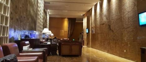 A hotel lobby with marble flooring, leather seating, a reception desk, and a television screen.