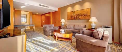 A hotel room with a sofa set, a coffee table, a flat-screen TV, and a painting on the wall.