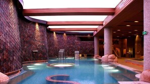 An indoor swimming pool with a unique design, featuring a central spiral and a stone wall on one side. - Blossom Seasons Club (Beijing)