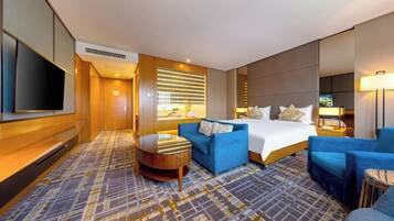 Habitación de hotel con cama, sofá azul, una pequeña mesa redonda y televisor montado en la pared.