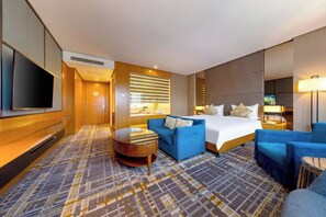 A hotel room with a bed, a blue sofa, a small round table, and a TV mounted on the wall. - Blossom Seasons Club (Beijing)