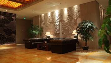 A lobby with a seating area, a large potted plant, and a textured wall.