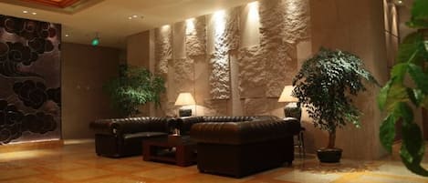 A lobby with a seating area, a large potted plant, and a textured wall.
