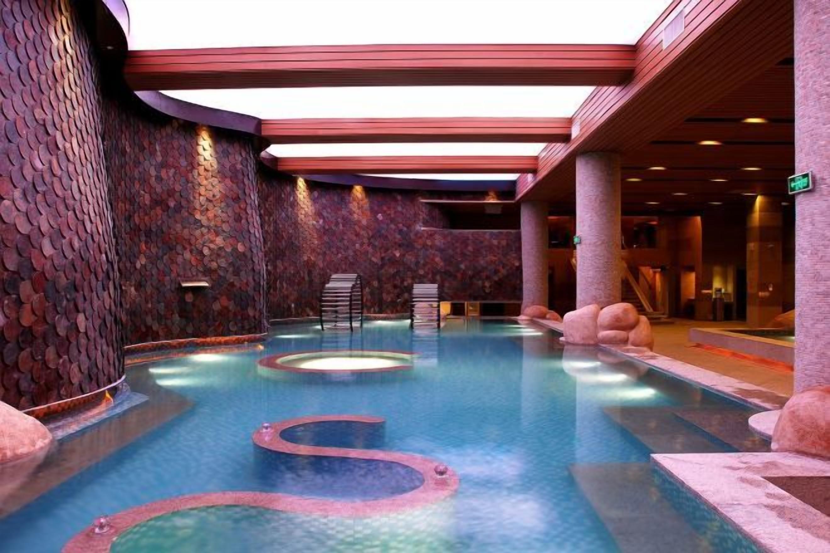 Una piscina interior con múltiples bañeras de hidromasaje, paredes de piedra y una zona de estar.