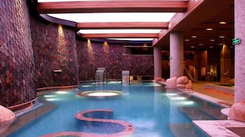An indoor swimming pool with multiple hot tubs, stone walls, and a seating area.