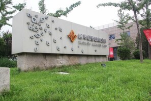 A sign with text and a logo, set against a grassy background with trees and a building in the distance. - Blossom Seasons Club (Beijing)