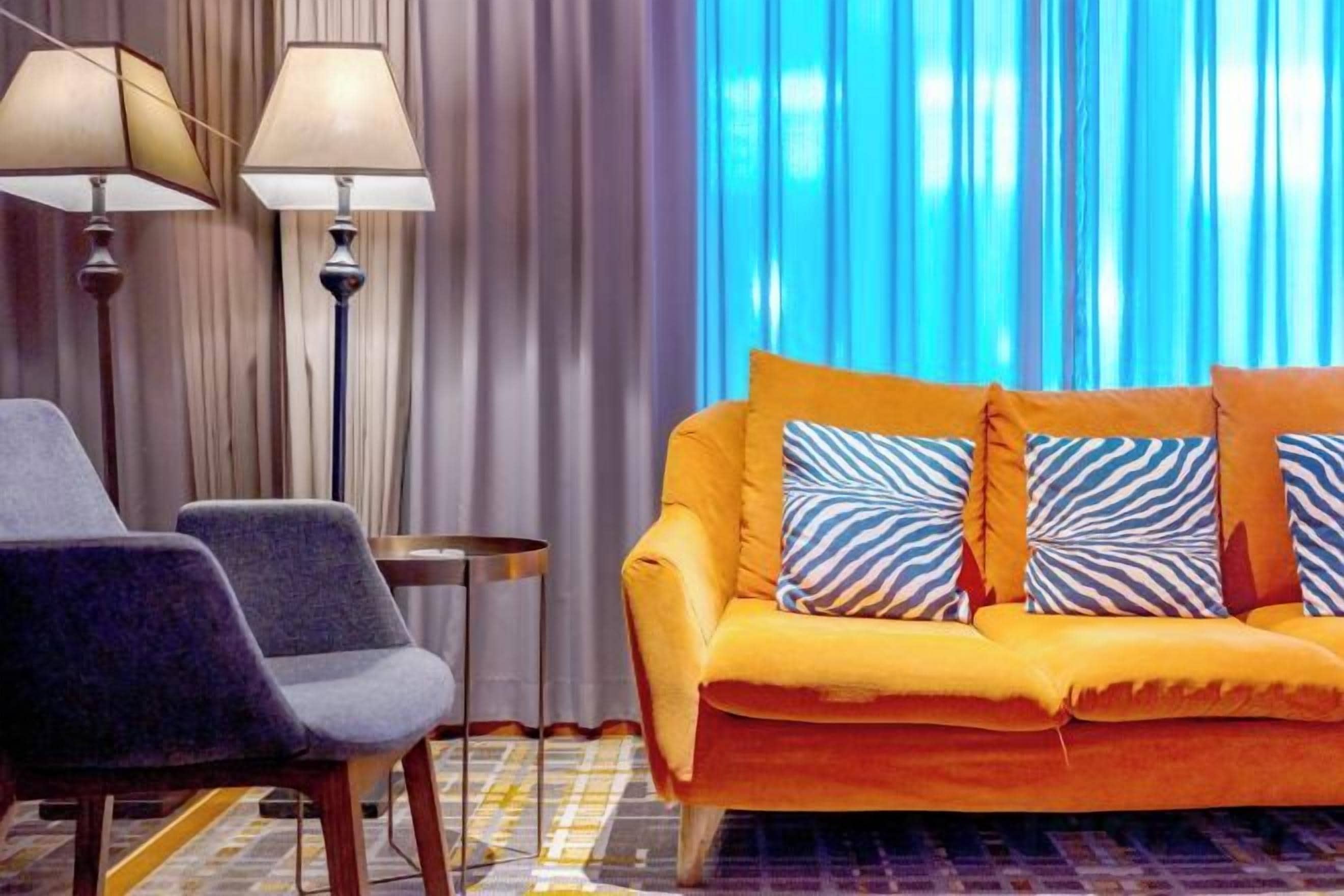 Una habitación con sofá, dos sillones, lámpara y cortina.