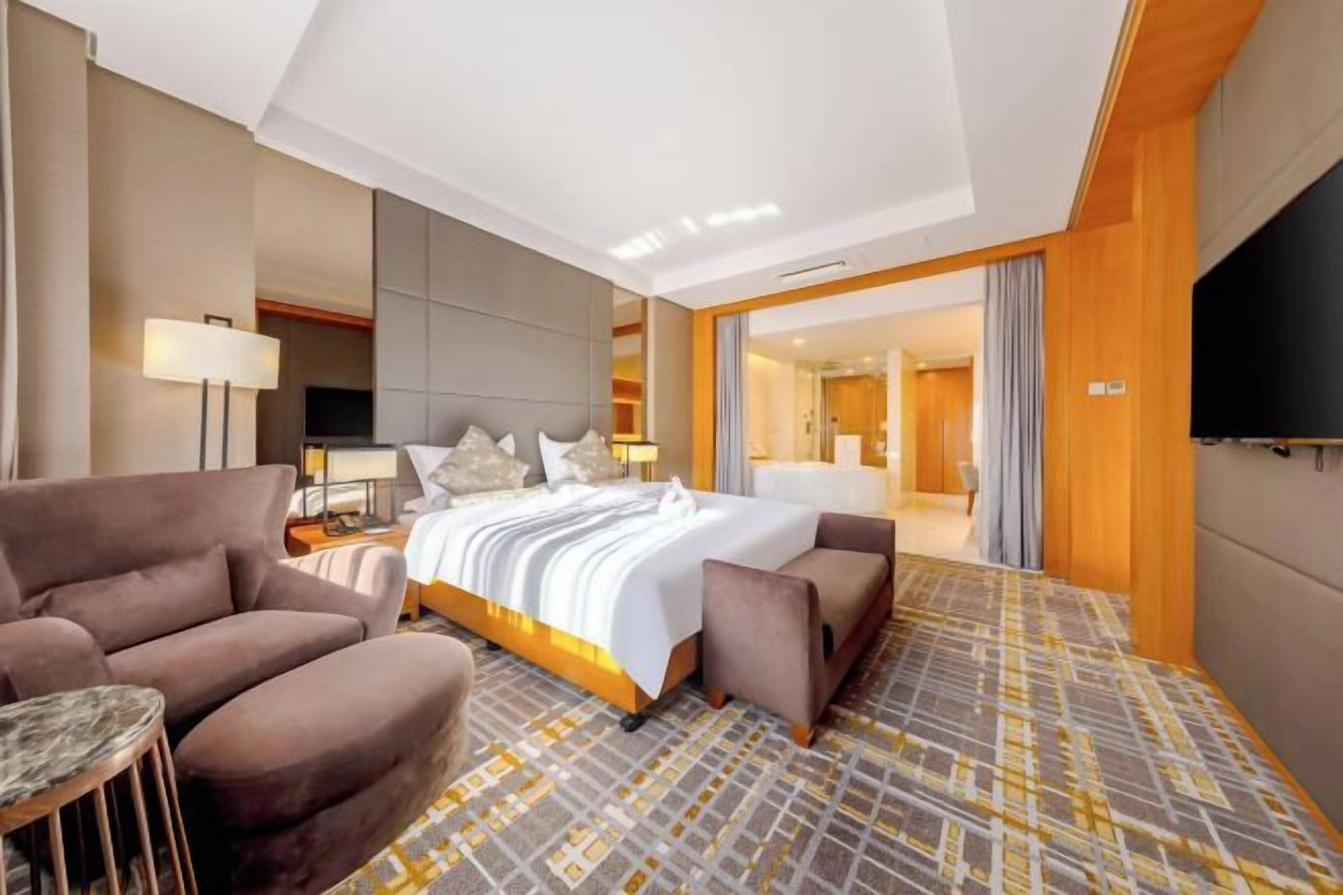 Ein Hotelzimmer mit einem großen Bett, zwei Sesseln, einem kleinen Tisch, einem Fernseher und einem gemusterten Teppich.