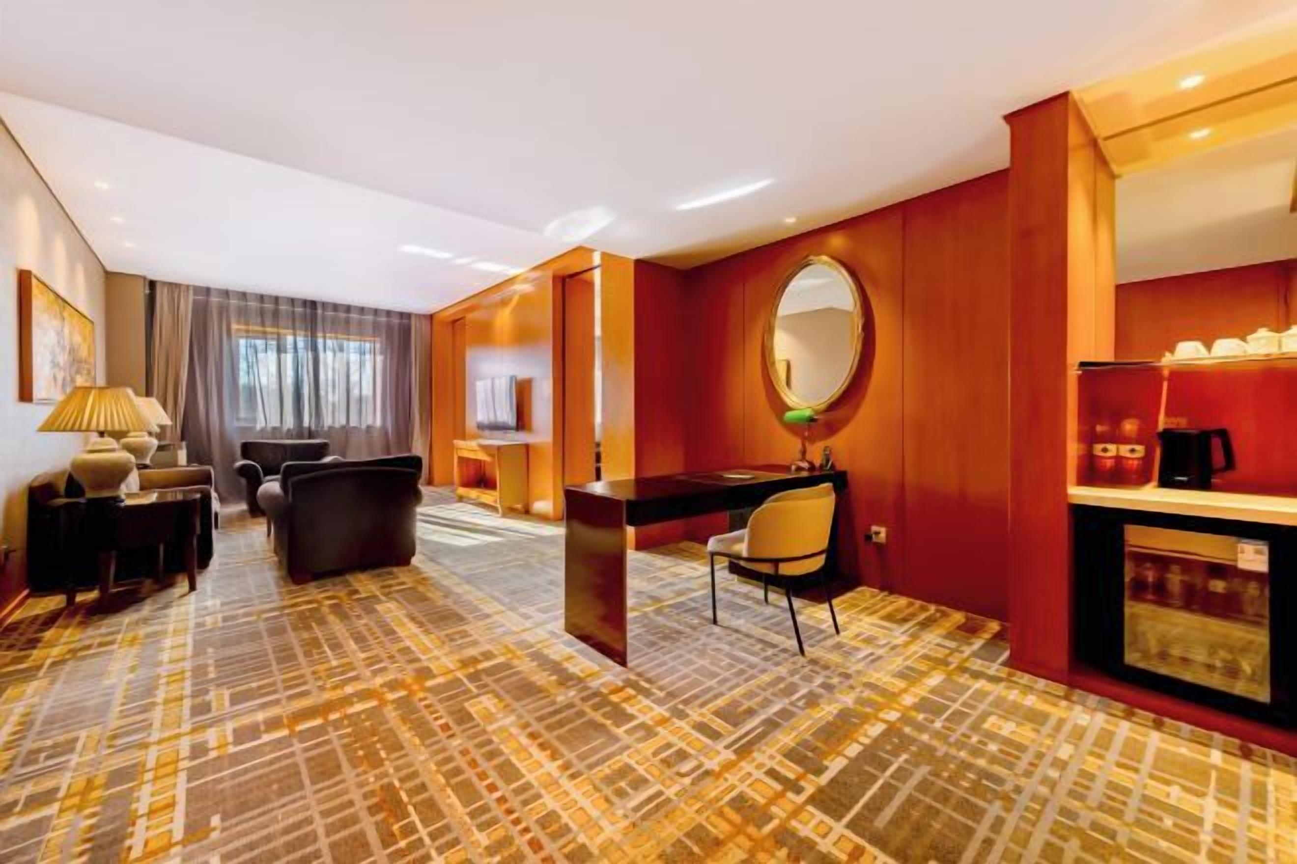 A hotel room with a large bed, a desk with a chair, a sofa, a coffee machine, and a television.