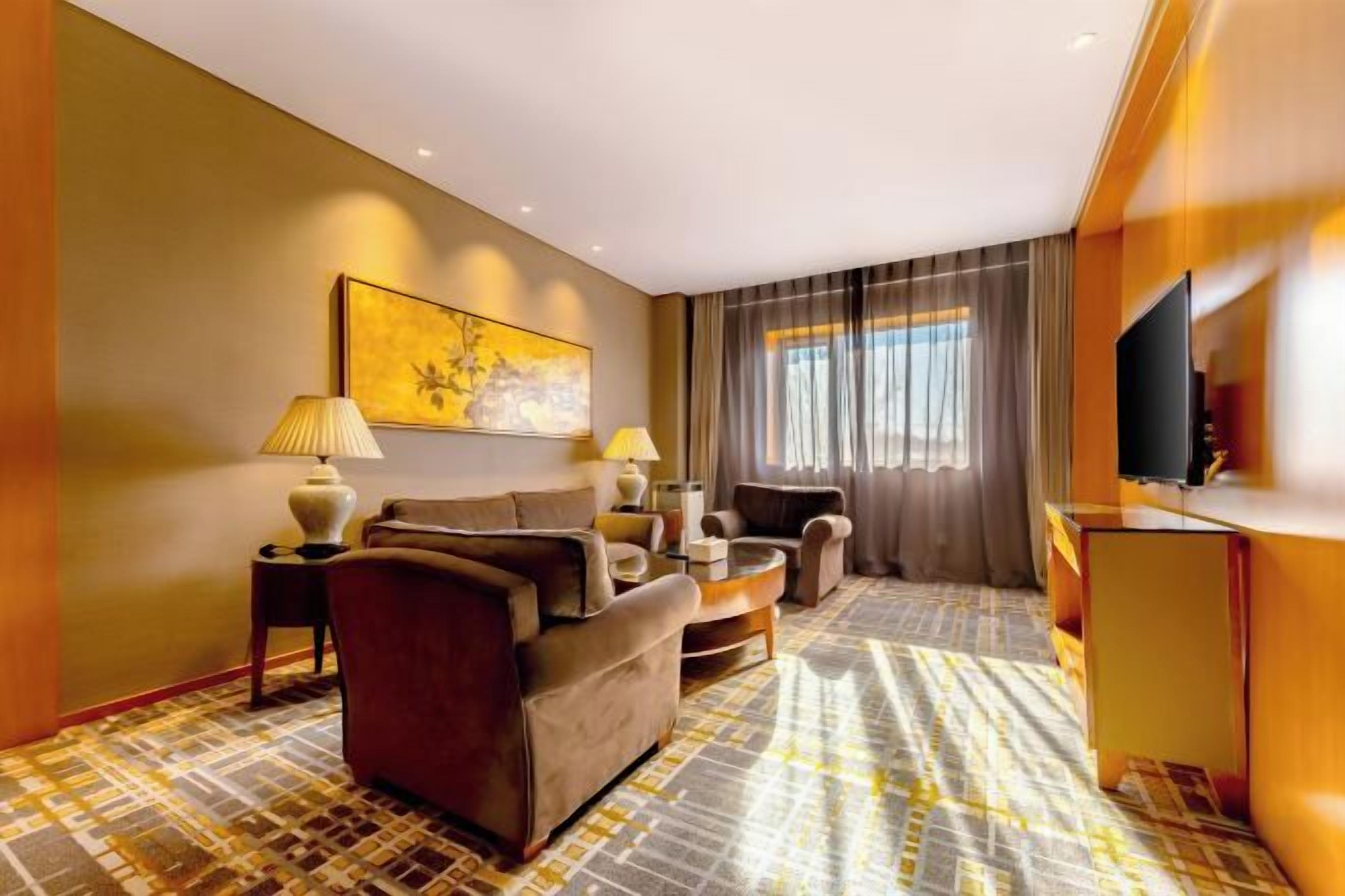 A hotel room with a sofa, armchairs, a coffee table, a TV, and a patterned carpet.