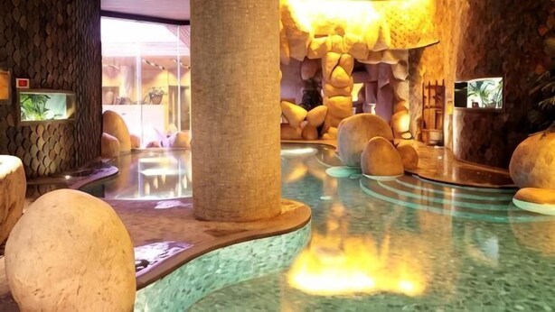 A spa area with a stone wall, a hot tub, and a small waterfall. - Blossom Seasons Club (Beijing)
