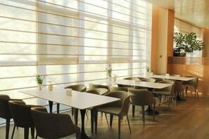 A spacious indoor dining area with multiple tables and chairs, large windows allowing natural light, and potted plants. - Blossom Seasons Club (Beijing)