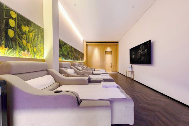 A modern spa room with massage chairs, a large wall mural, and a television.