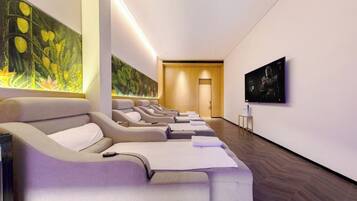 A modern spa room with massage chairs, a large wall mural, and a television.