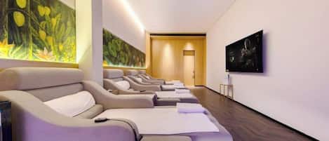 A modern spa room with massage chairs, a large wall mural, and a television.