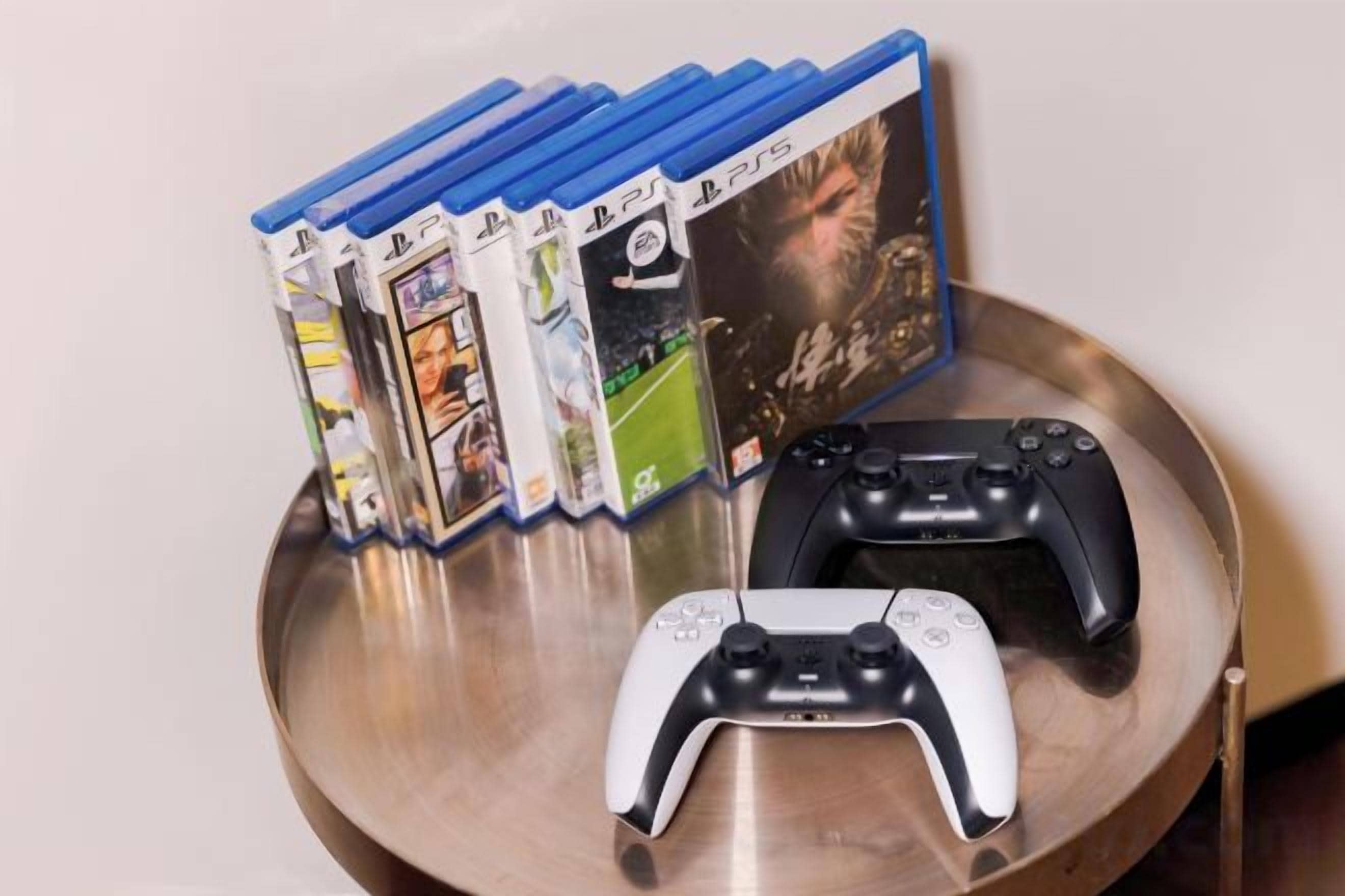 Una colección de cajas de juegos de PlayStation y dos mandos de PlayStation sobre una mesa metálica redonda.