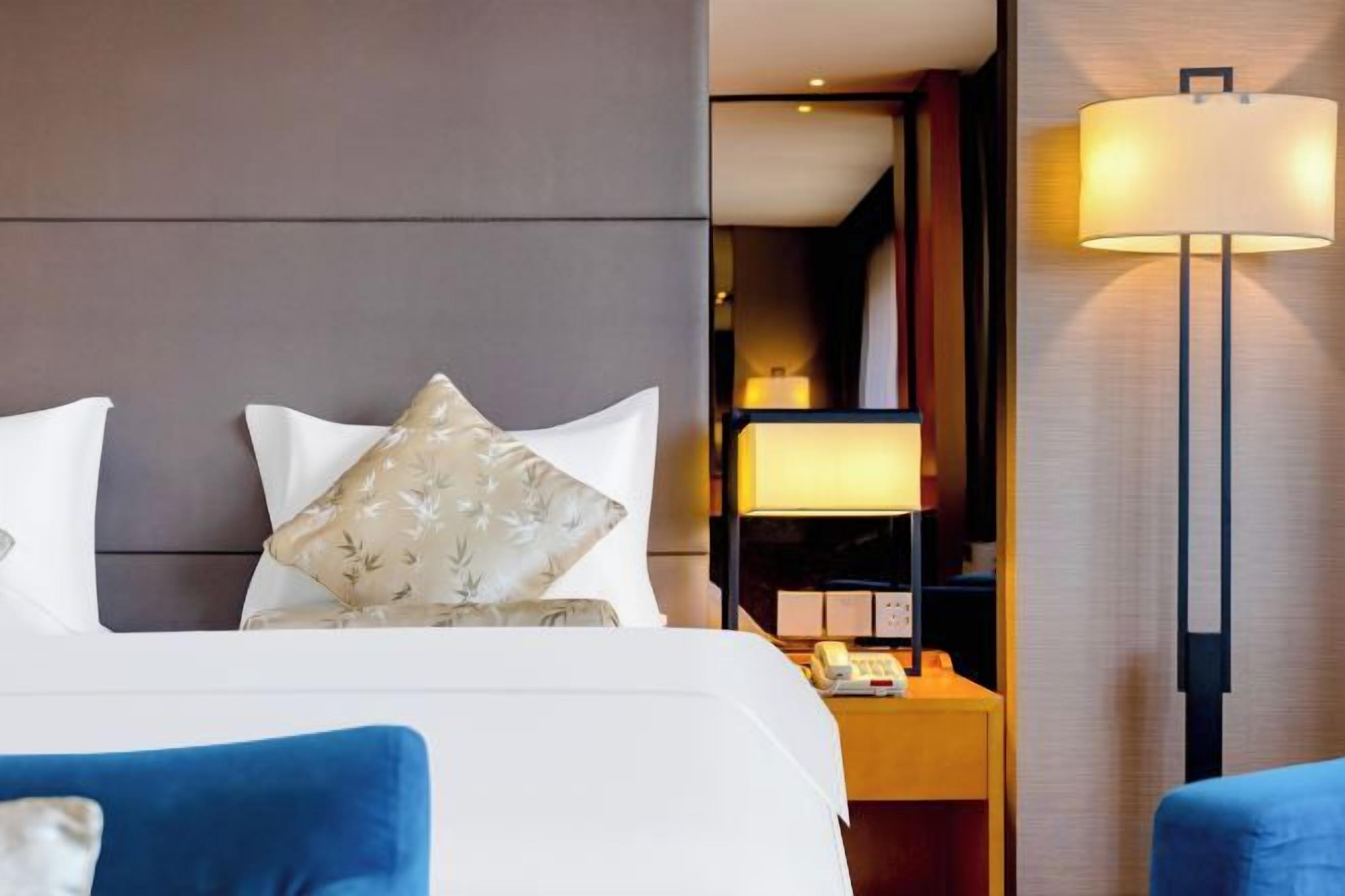 A hotel room with a bed, pillows, a nightstand, a lamp, and a blue chair.
