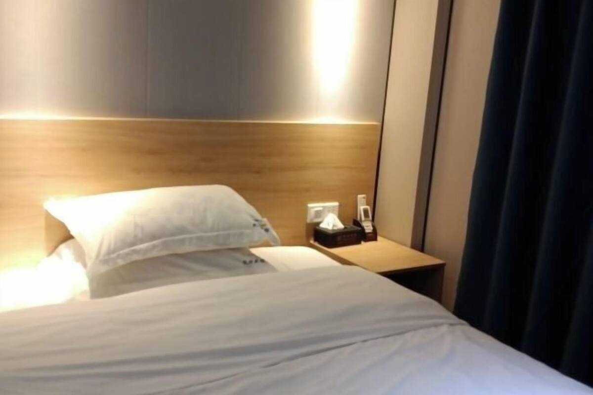 A hotel room with a bed, a bedside table with a lamp, and a nightstand with a phone.